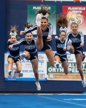 South cheerleaders in navy uniforms leap high into the air in perfect synchronization during a competitive cheerleading routine.