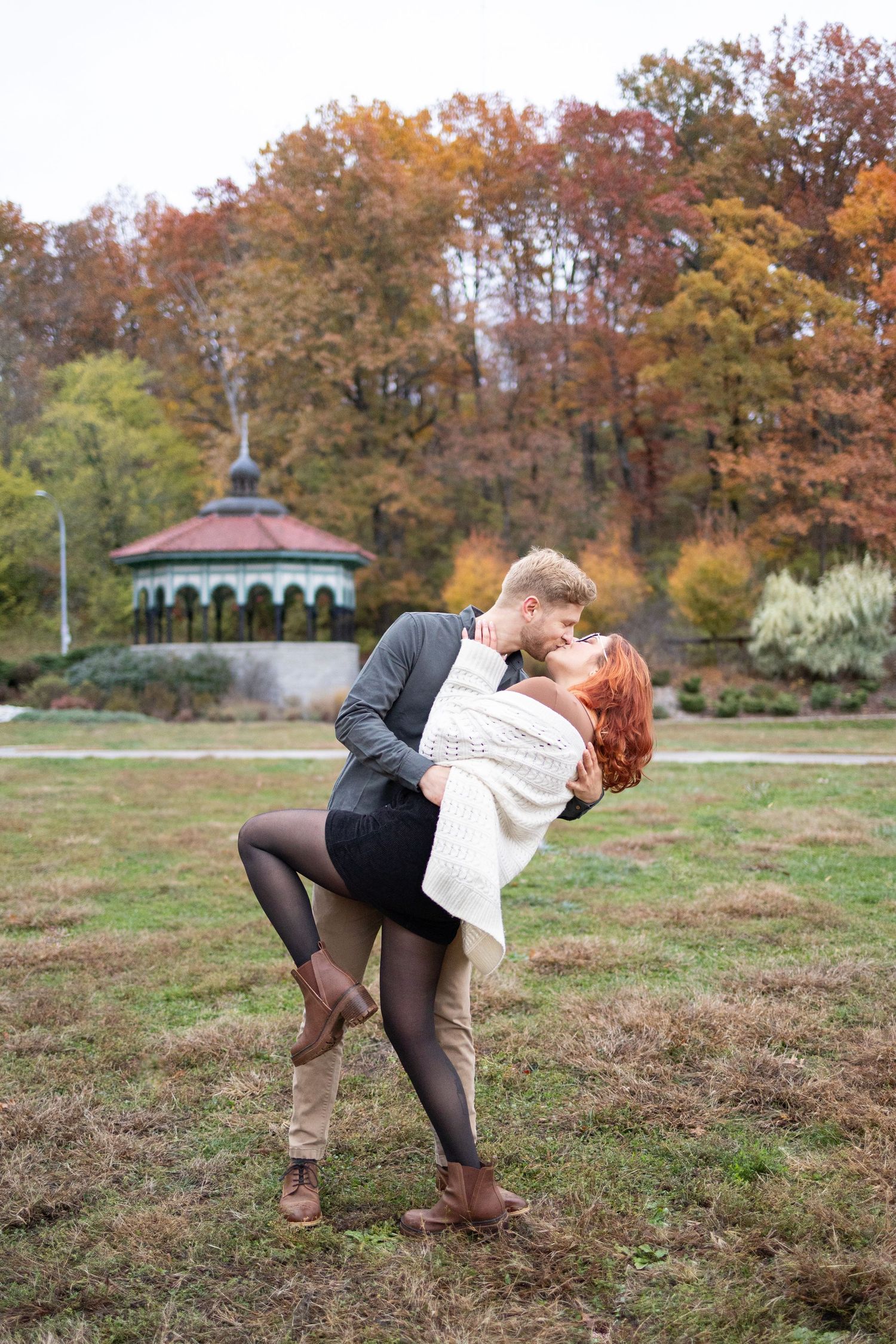 Couple sharing a romantic dip kiss in Eden park with colorful trees and a gazebo in the background.