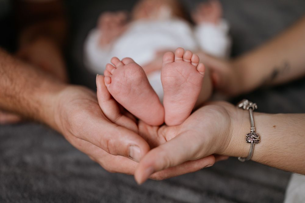 Two parents cradling their newborn baby's tiny feet in their hands, mother wearing charm bracelet.