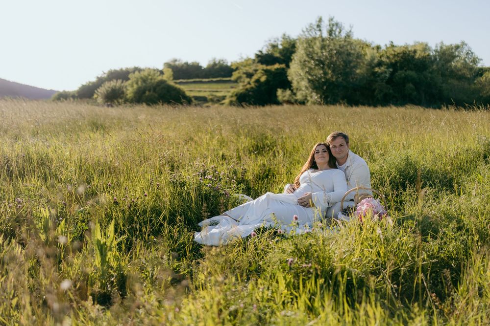 Couple relaxing together in sunny green meadow field during maternity photo session.