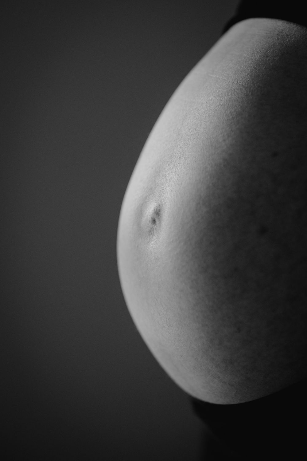 Black and white close-up photo of a pregnant woman's bare baby bump against a dark background.