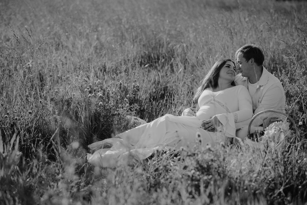 Black and white romantic couple kissing while lying in tall grass field.