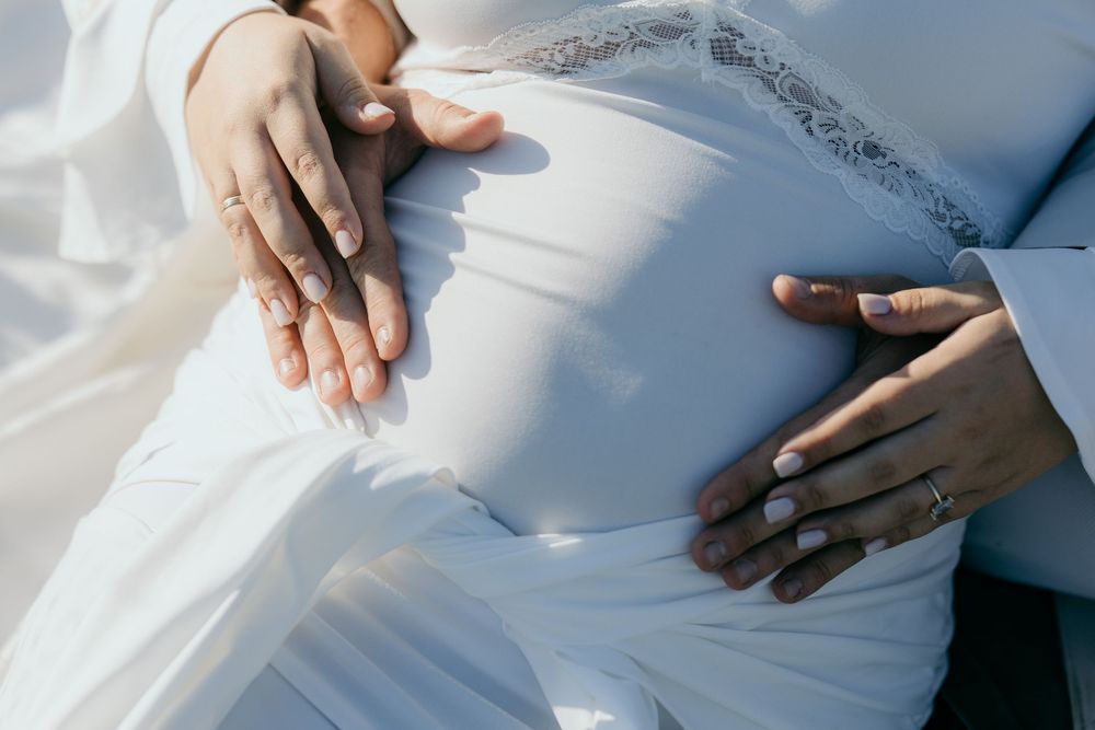 Close-up of couple's hands tenderly cradling pregnant belly in white maternity dress.