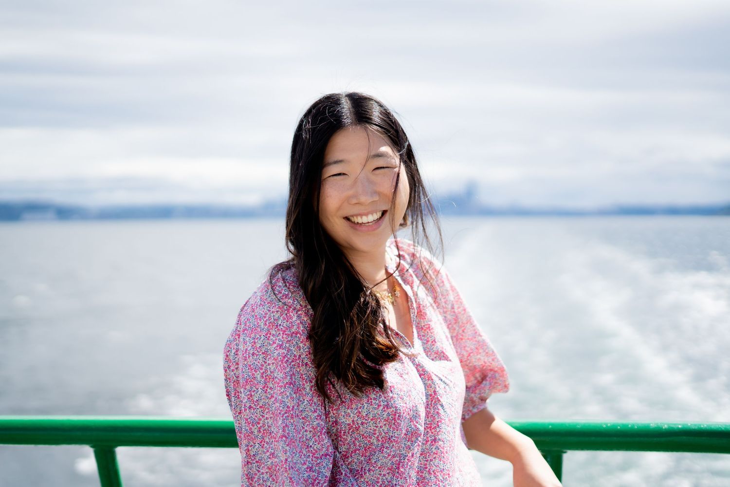 Smiling young Asian woman in a colorful red and pink star-print top posing outdoors.