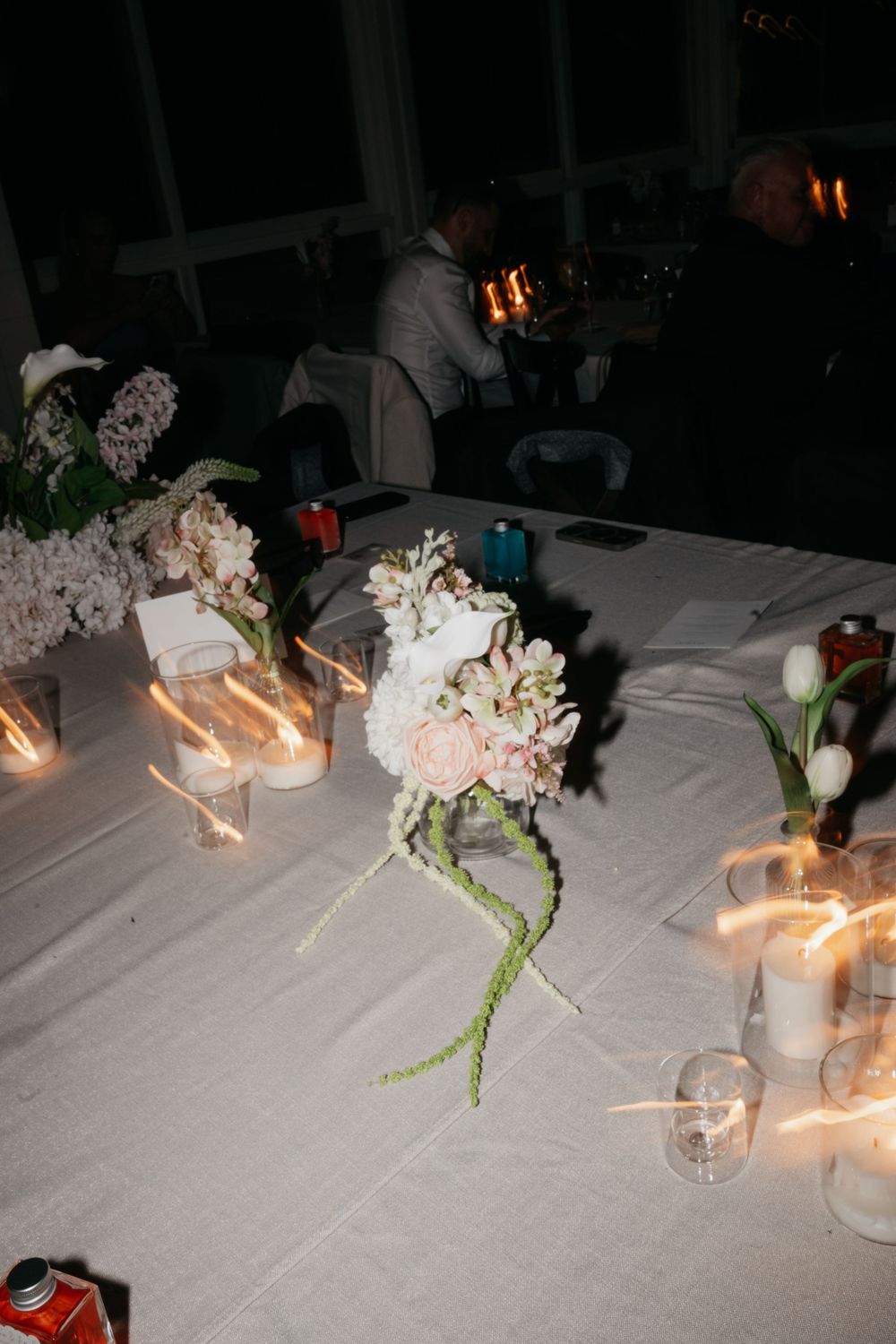 Romantic candlelit wedding reception table featuring blush floral centerpiece with trailing greenery in dim evening light.