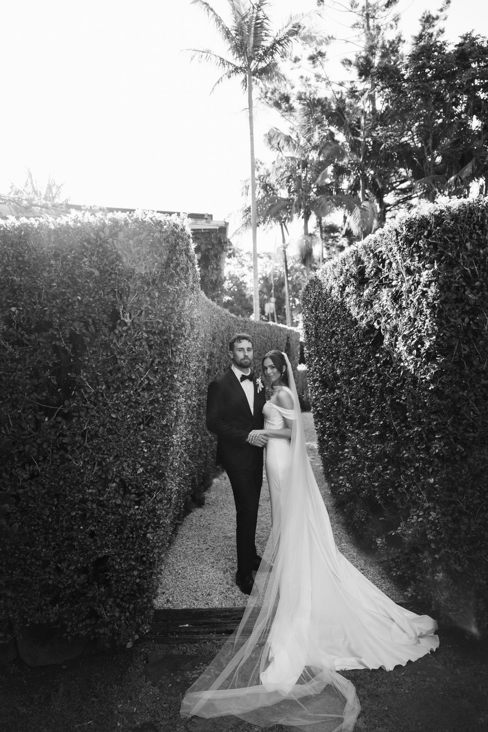 Black and white photo of bride and groom posing in a lush garden hedge maze on their wedding day.