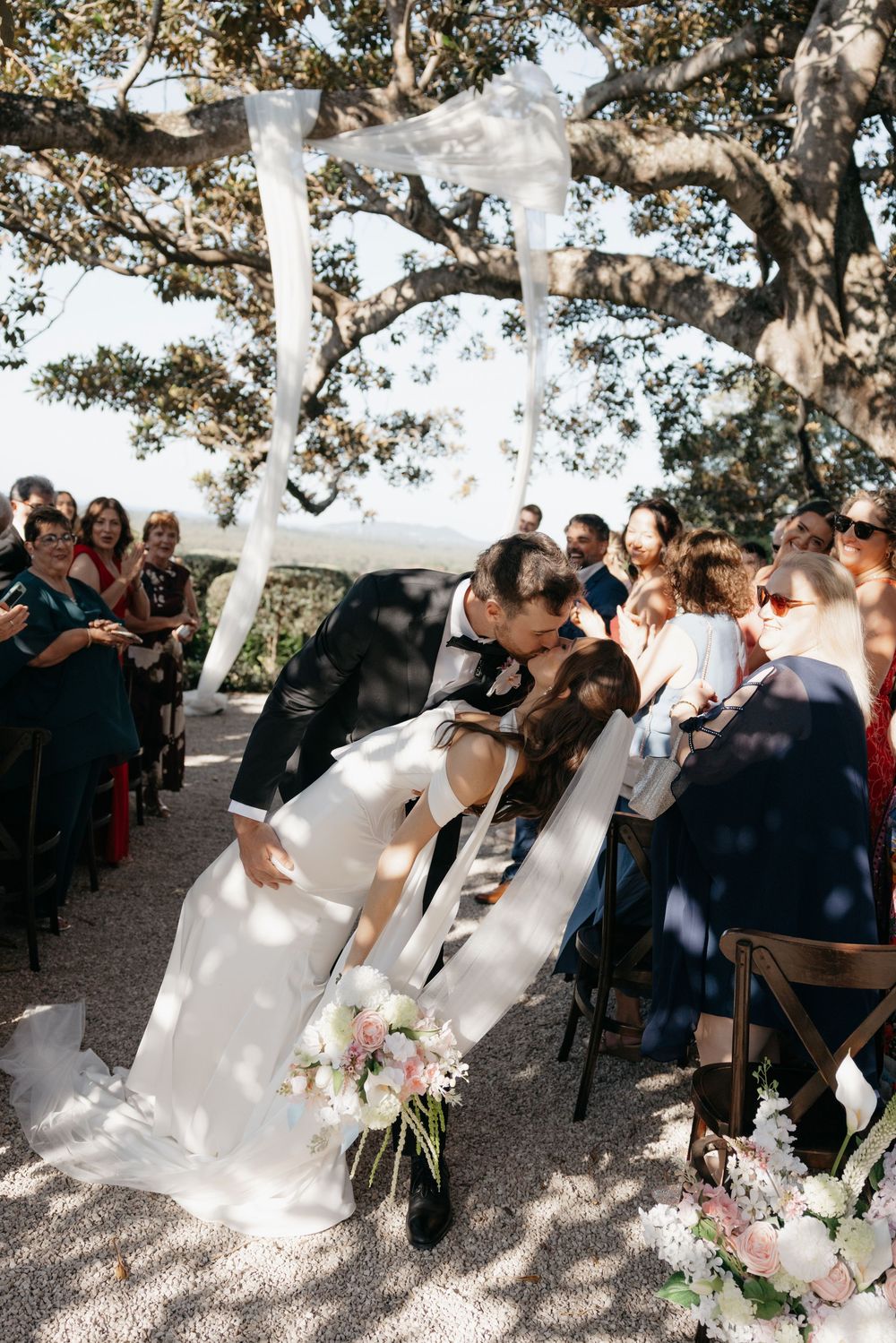Bride and groom share a romantic dip kiss at the altar during their outdoor wedding ceremony.