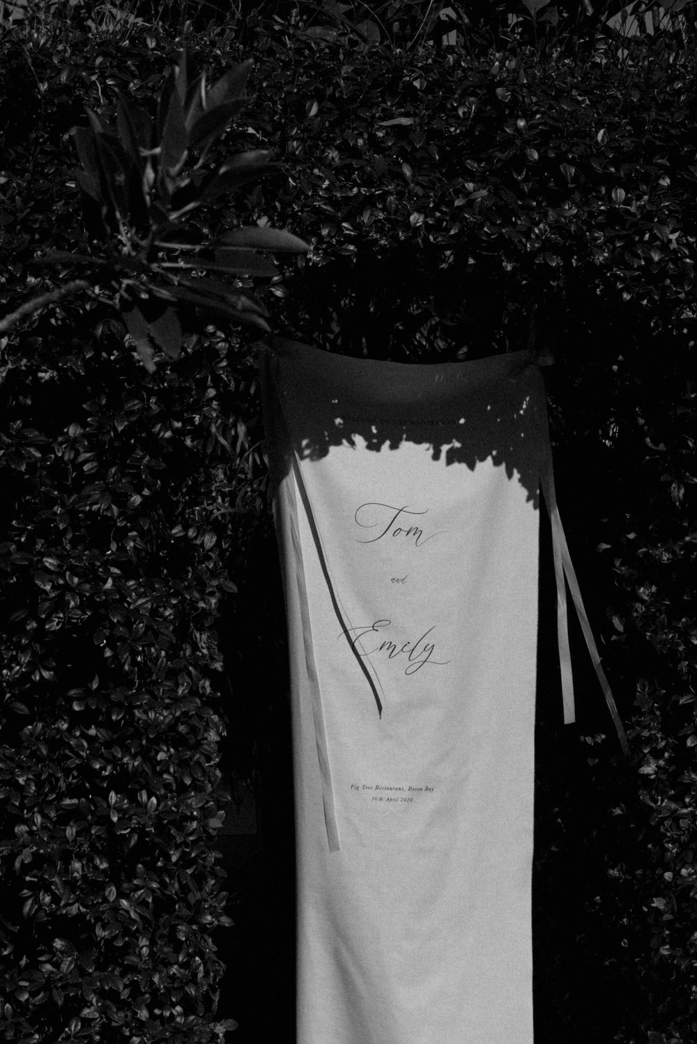 Black and white wedding welcome sign reading Tom and Emily displayed against lush garden hedges.