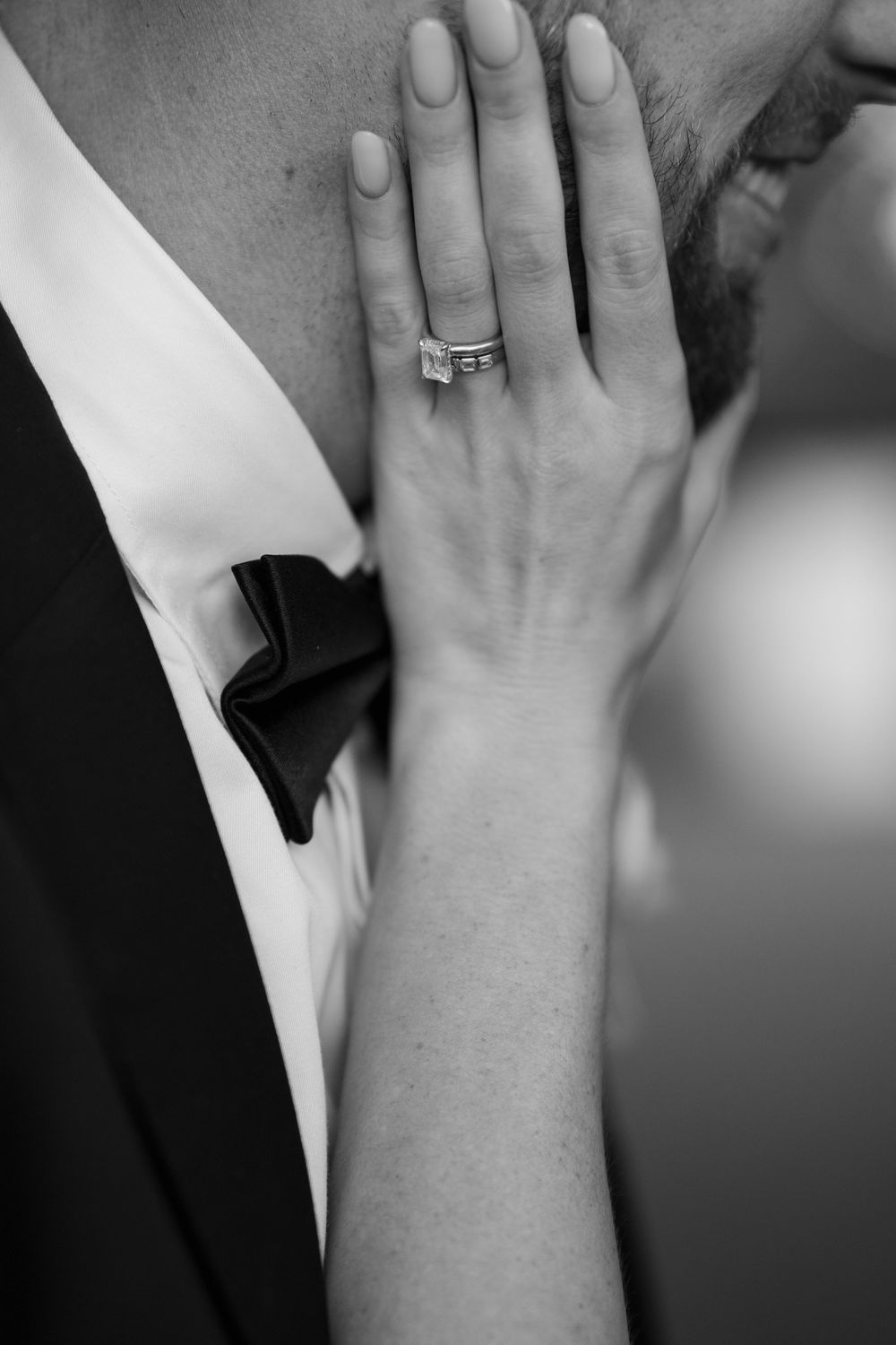 Black and white close-up of bride's hand with emerald cut engagement ring resting on groom's chest.