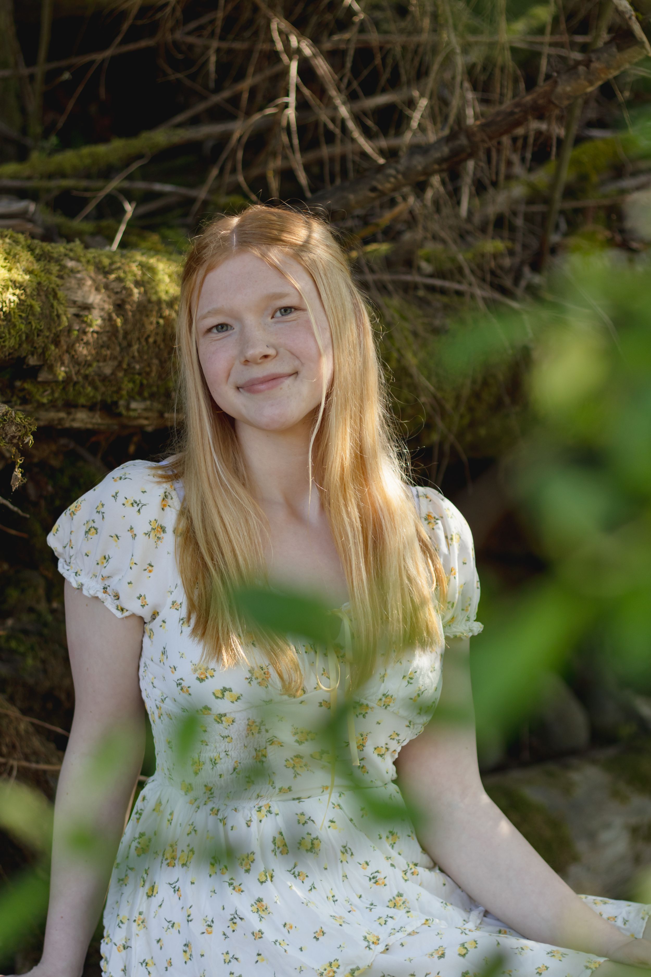Smiling young girl with blonde hair wearing a white floral dress sitting outdoors at little mashel river taken by pierce county photographer