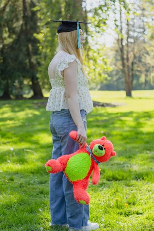 Blonde senior girl holding a teddy bear and wearing a graduation cap in a sunny Eatonville park taken by Washington photographer