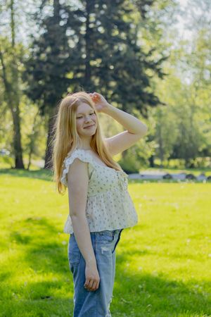 Happy blonde teenage girl in floral top and jeans posing in a sunny Eatonville Washington park taken by pierce county photographer