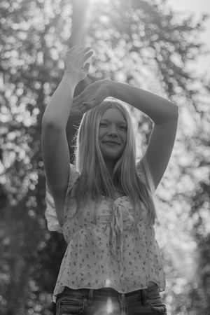 Black and white portrait of a girl with arms raised above her head in a sunlit forest in Eatonville Washington taken by Roy photographer