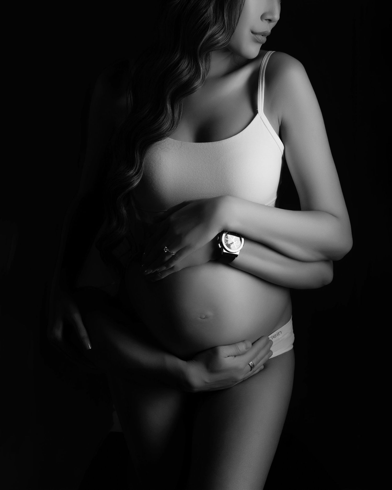 Black and white maternity photo emphasizing pregnancy curves with minimalist styling.