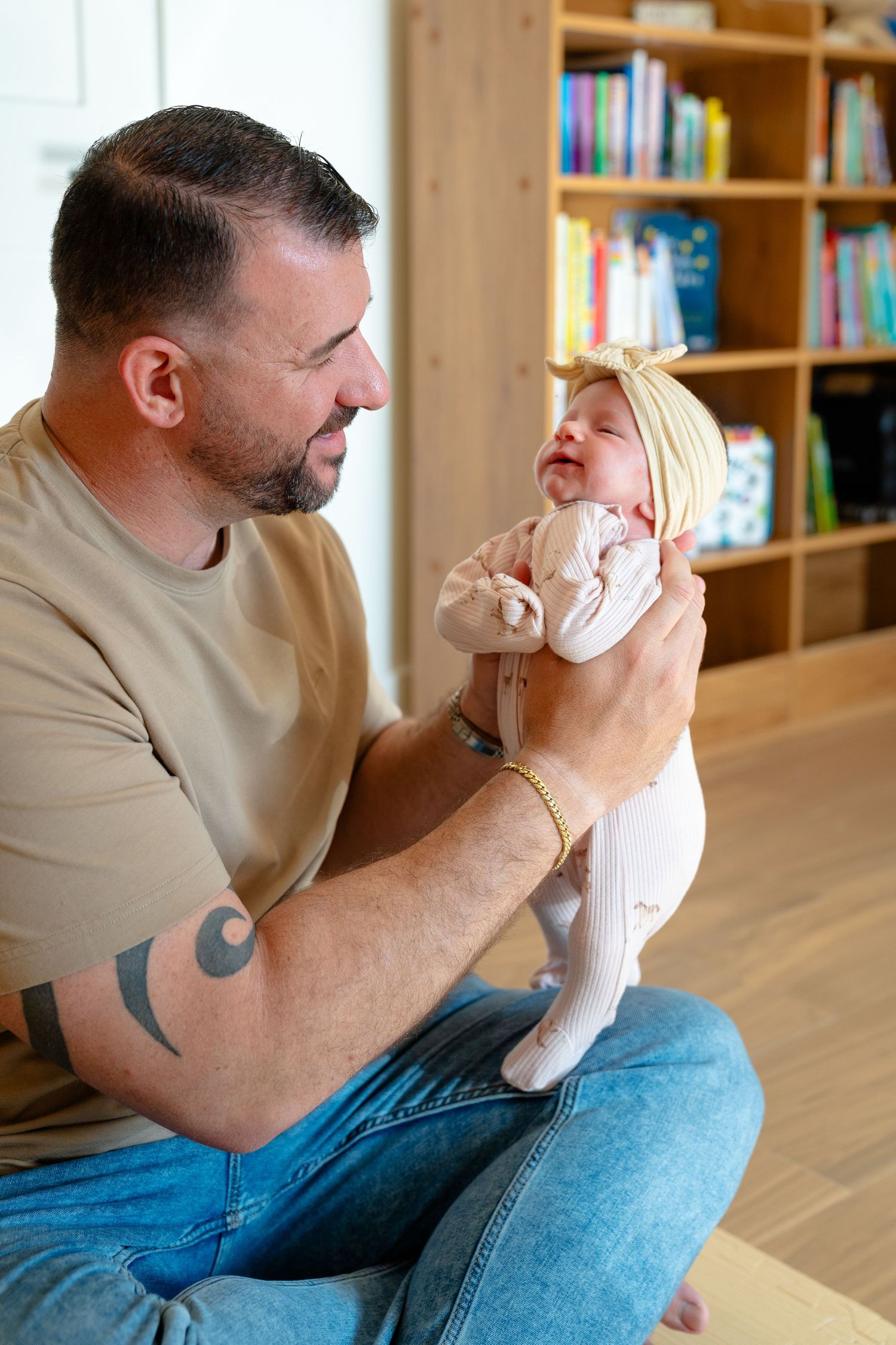 A father sitting cross-legged on the floor, lovingly holding his smiling baby girl wearing a bow headband.