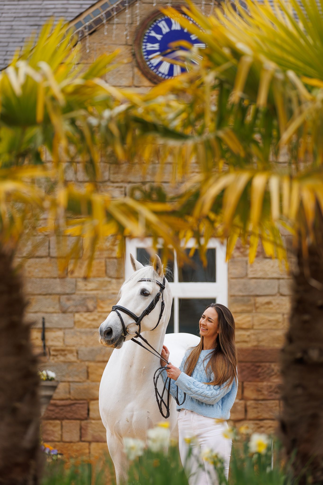 A brown horse and rider in a white sweater pose together against autumn foliage in soft natural lighting.
