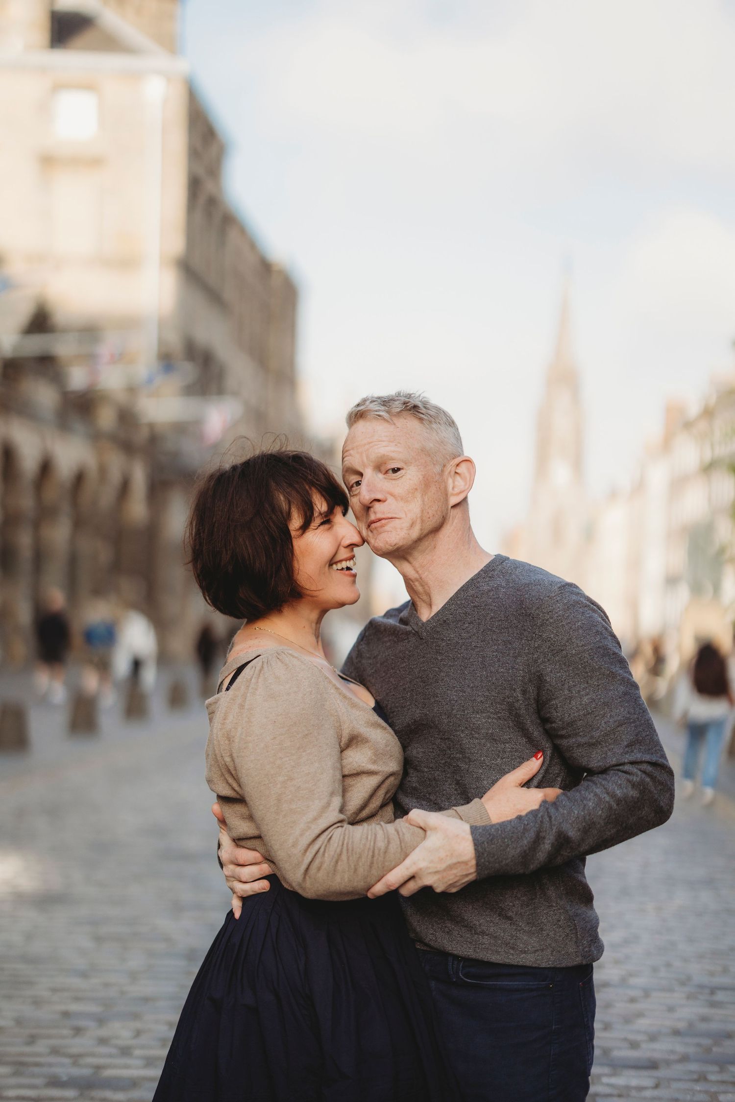 A happy middle-aged couple embracing on a cobblestone street in a historic European city.