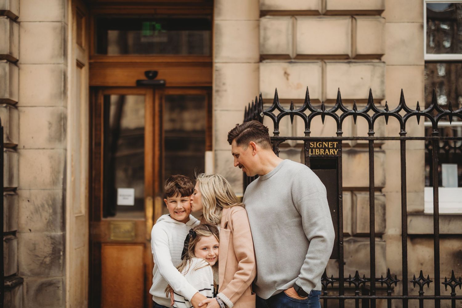 Family of four sharing a warm embrace outside the Signet Library in Edinburgh, Scotland.