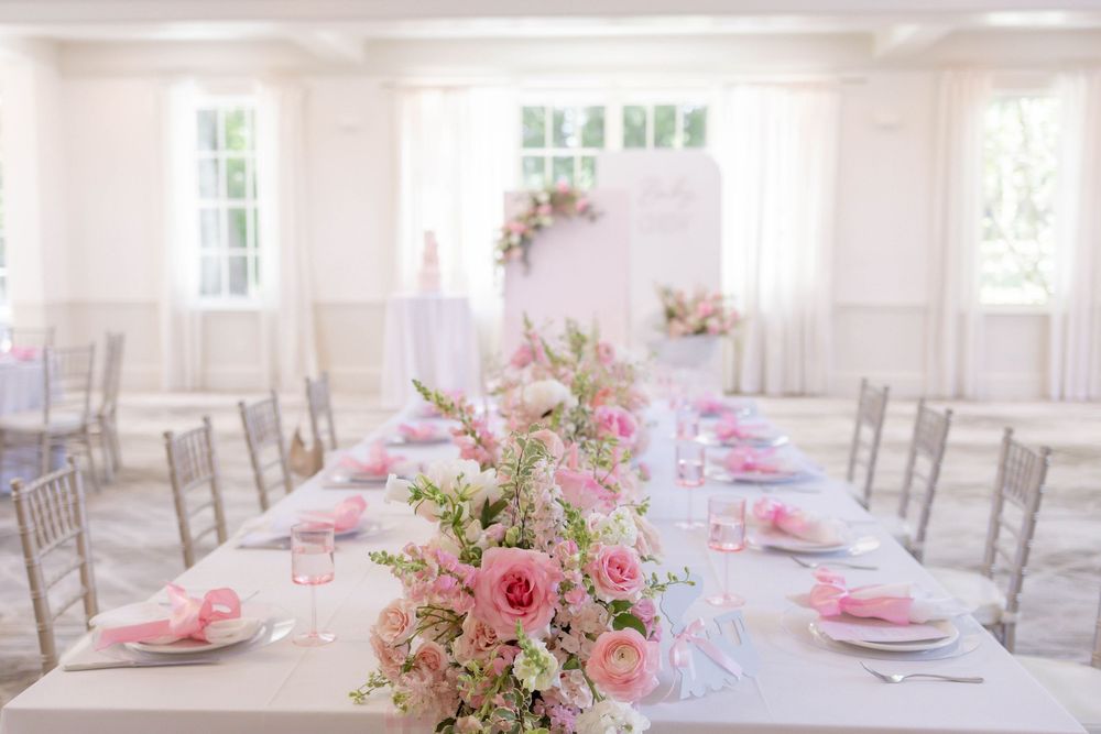 Elegant wedding reception table with pink floral centerpiece, silver chairs, and soft white decor in a bright airy venue.
