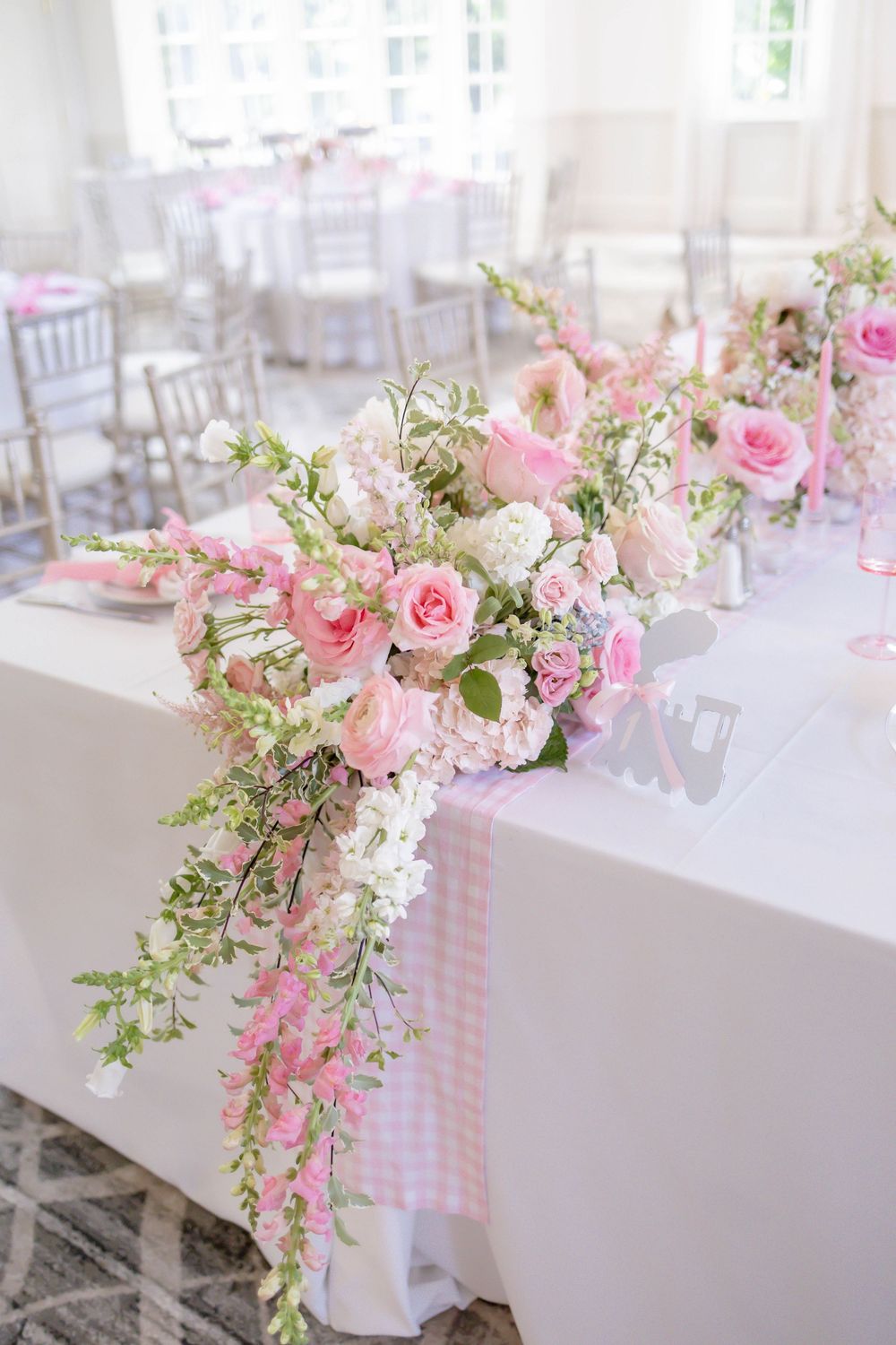 Elegant table adorned with cascading pink roses and white floral arrangements on a white linen tablecloth.