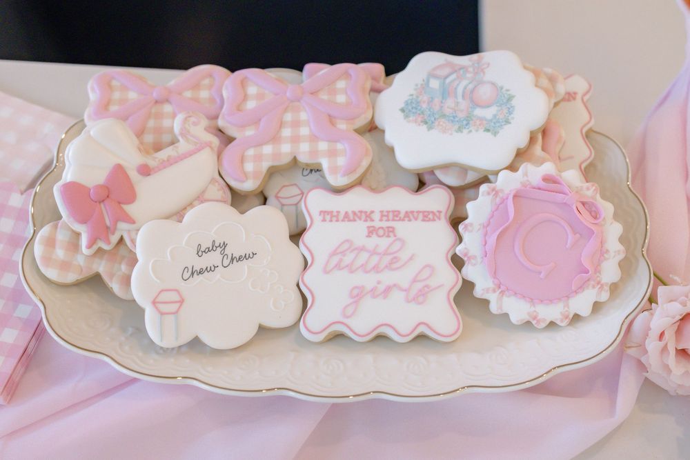 Pink baby shower decorated sugar cookies on a white plate, featuring butterfly, elephant, and girl-themed designs.