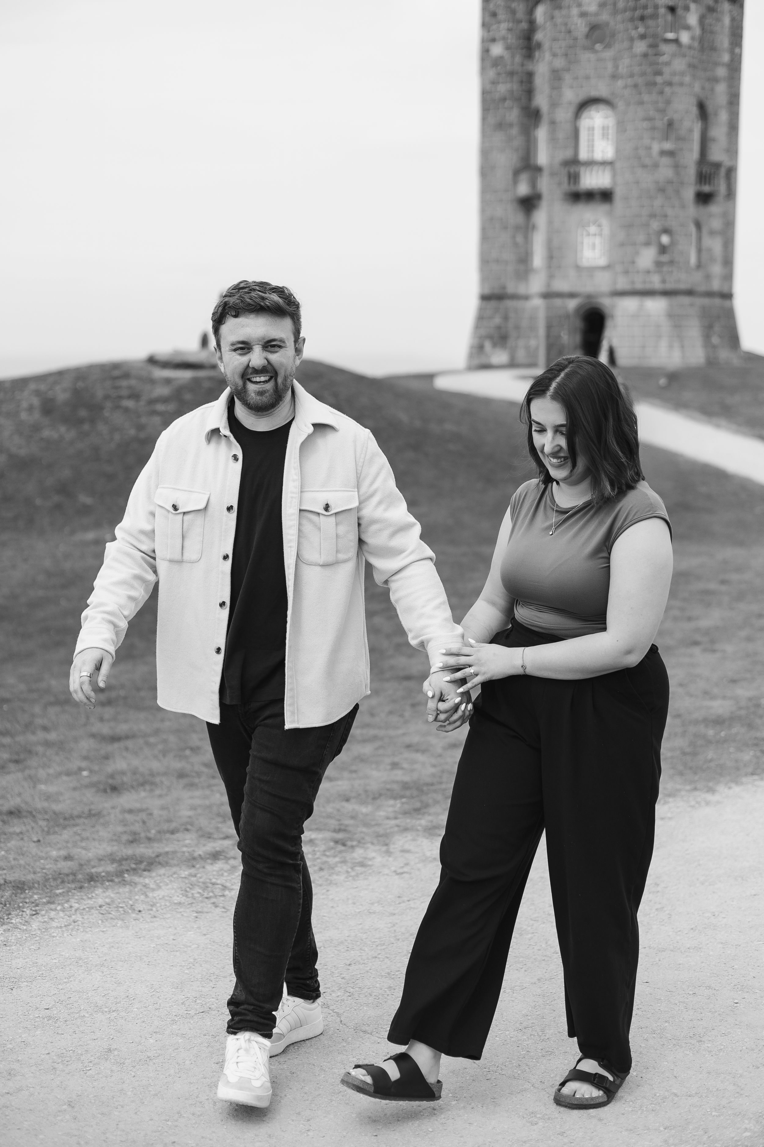 An engagement couple holding hands and walking around Broadway Tower for their proposal photoshoot.