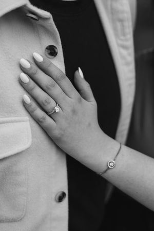 Close-up black and white photo of a womans hand displaying a diamond engagement ring and bracelet at Broadway Tower, Cotswolds.