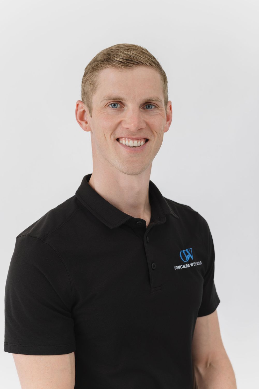 Smiling man in black Concorde Wellness polo shirt poses for professional headshot photo against white background.
