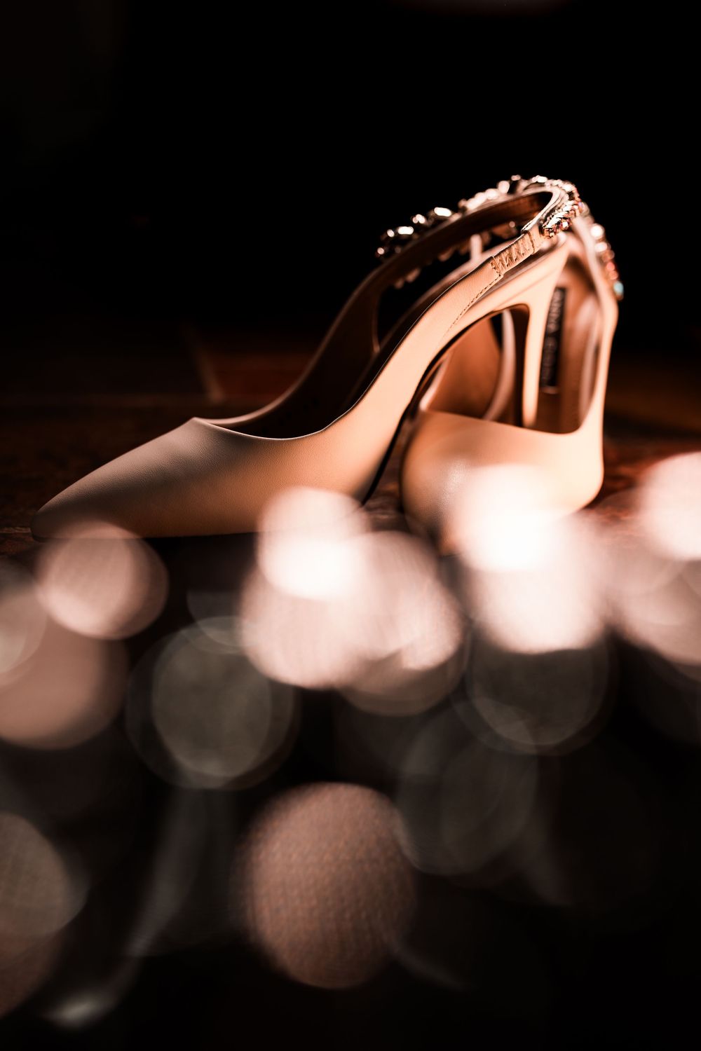 Close-up of embellished bridal heels with pearl details and beautiful bokeh light background.