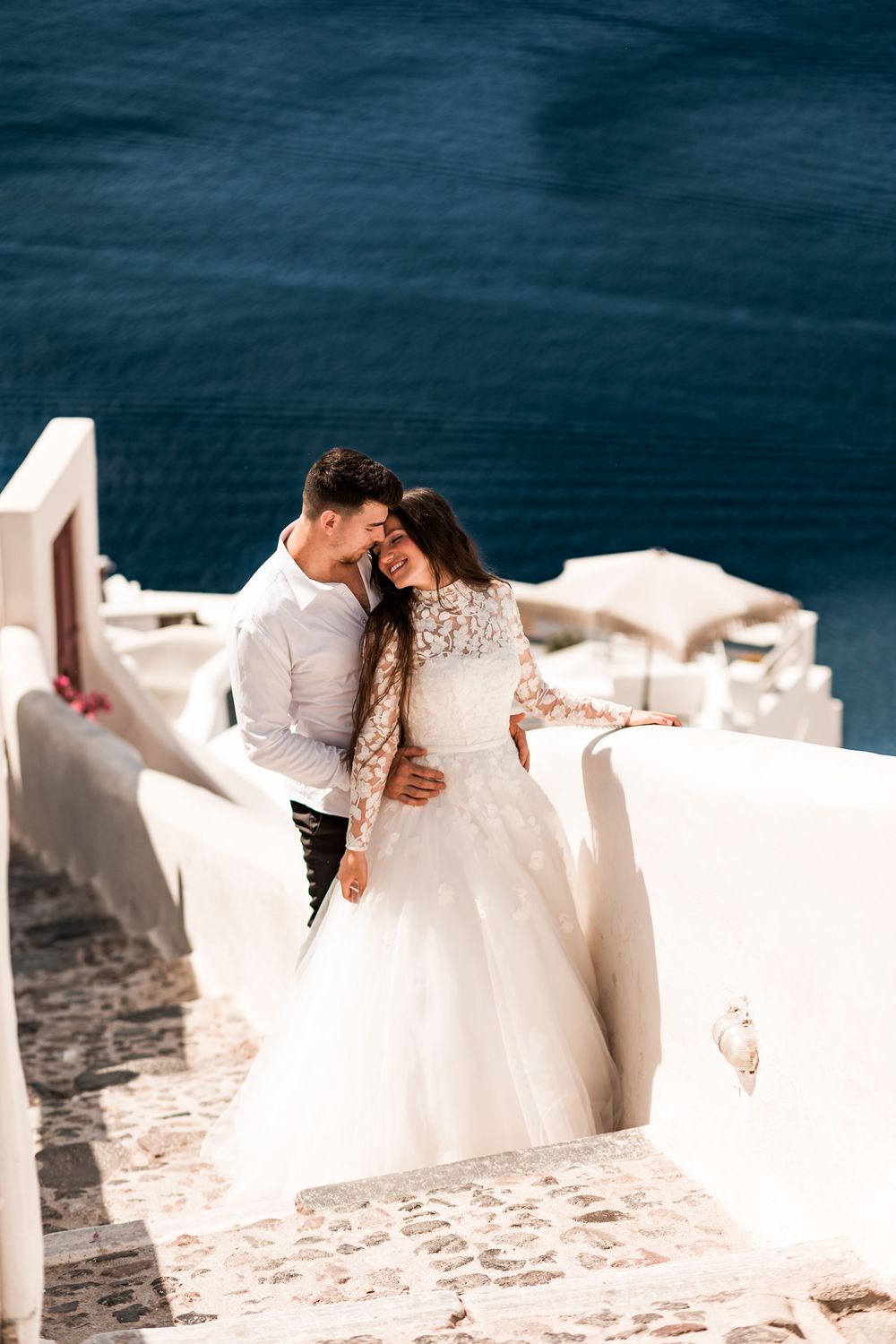 Happy couple embracing on white Santorini steps with deep blue sea behind them.