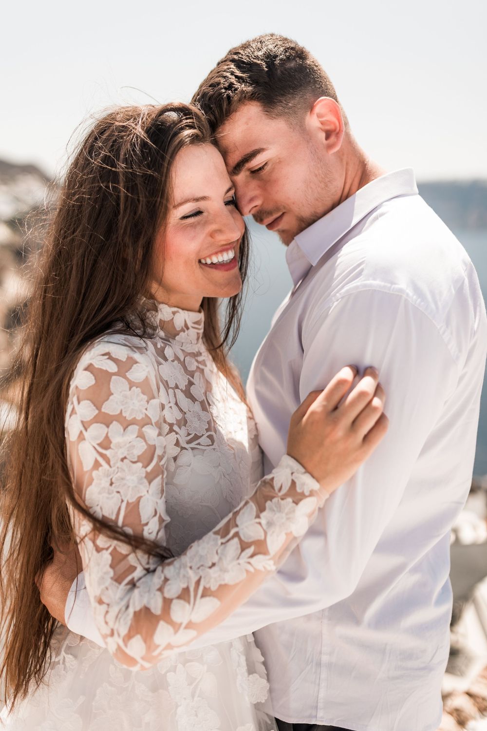 Happy newlyweds in close embrace smiling together on sunny Santorini wedding day.