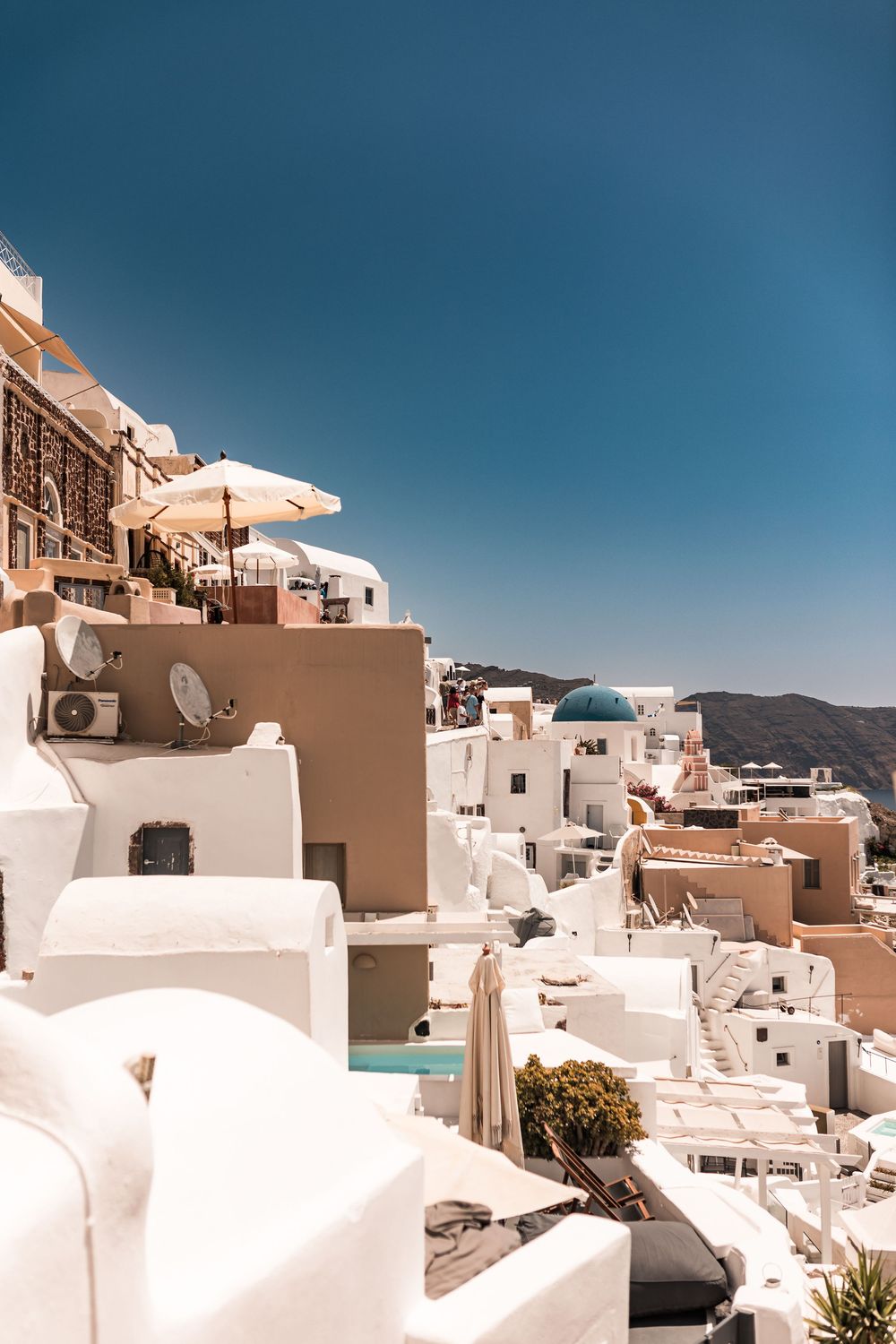 Whitewashed buildings and blue-domed churches cascade down the cliffs of Santorini, Greece under a clear blue sky.