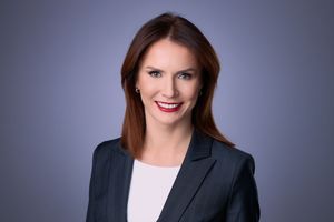 Professional woman in dark blazer with red lips smiling confidently against a gray studio background.