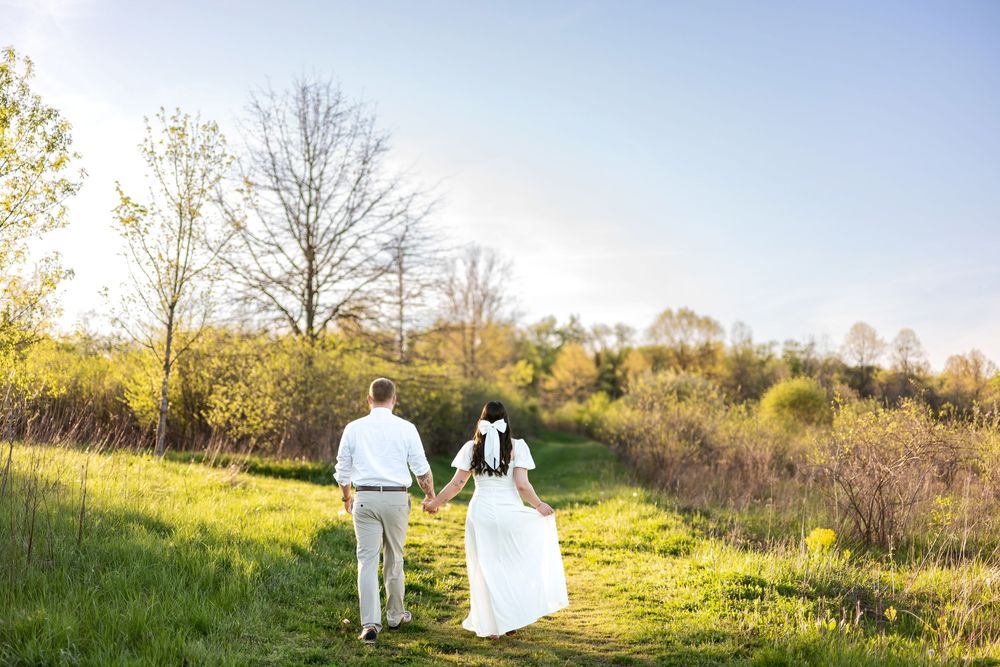 Couple walking hand in hand through green meadow at sunset.