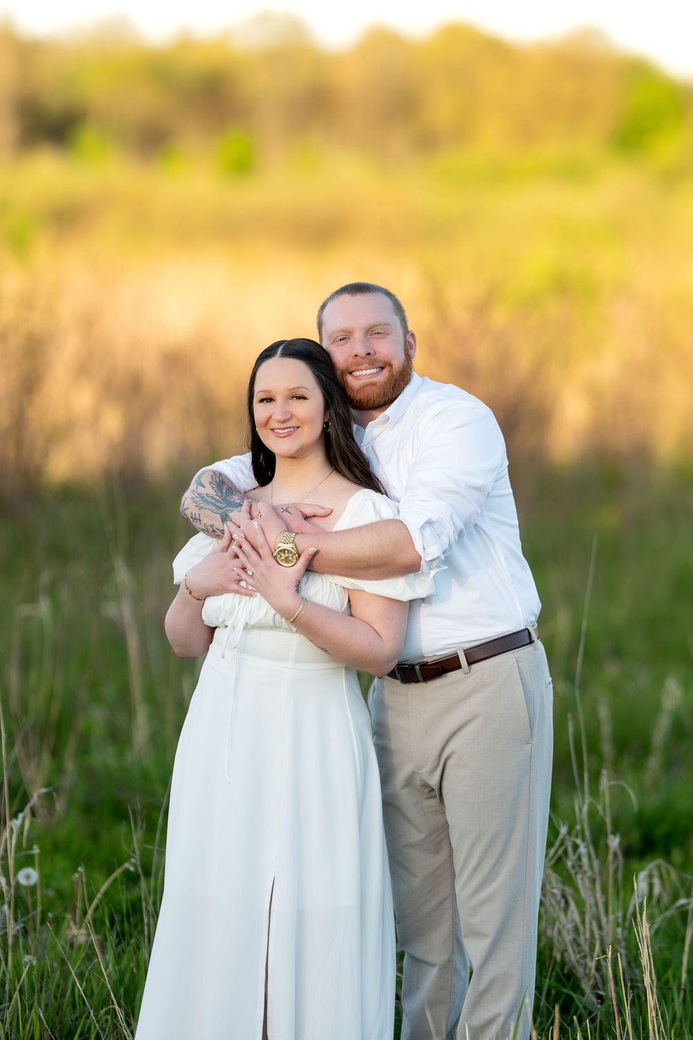 Smiling couple embracing in a golden sunlit field at sunset.