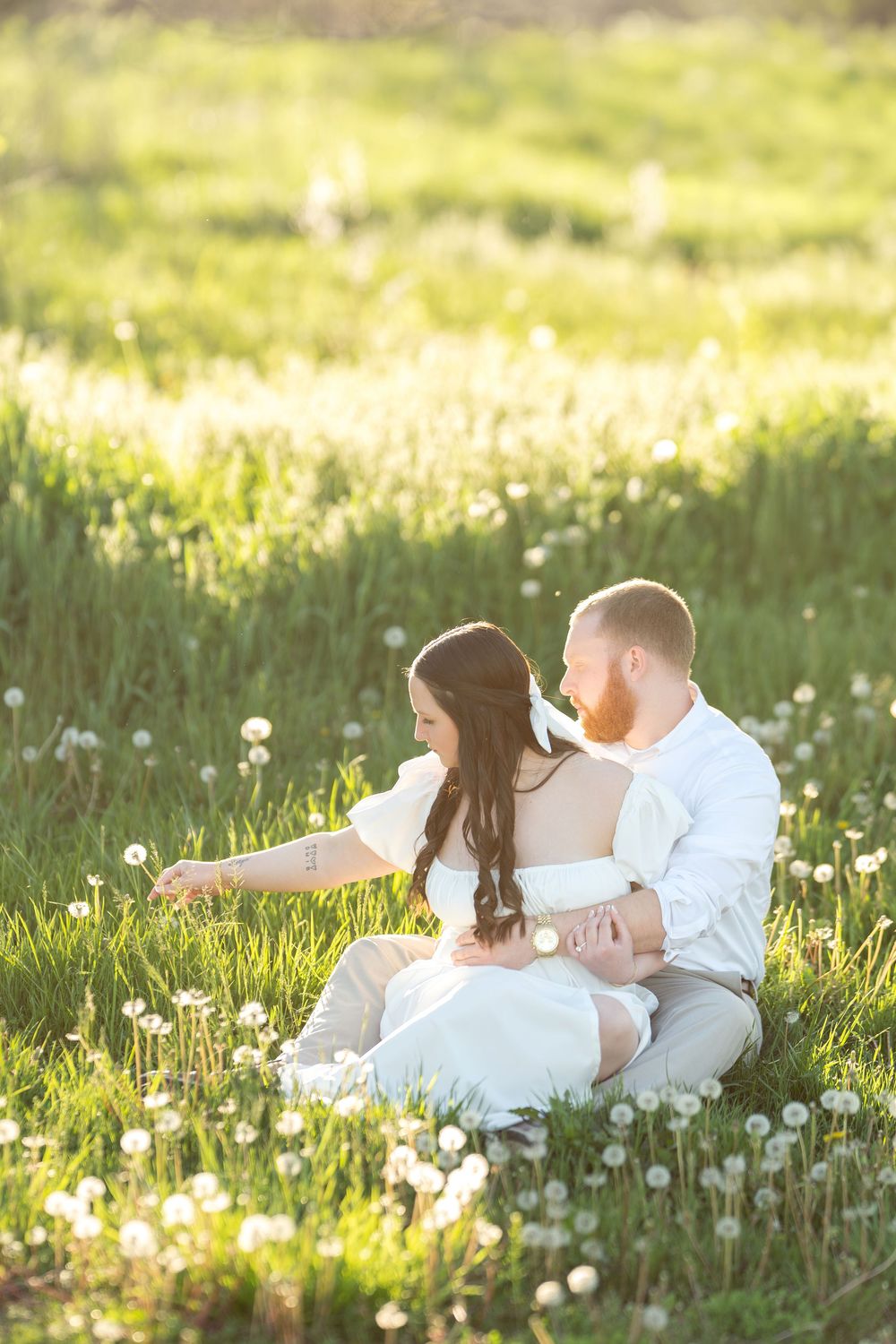 Couple sitting together in a lush green dandelion field during golden hour sunset.