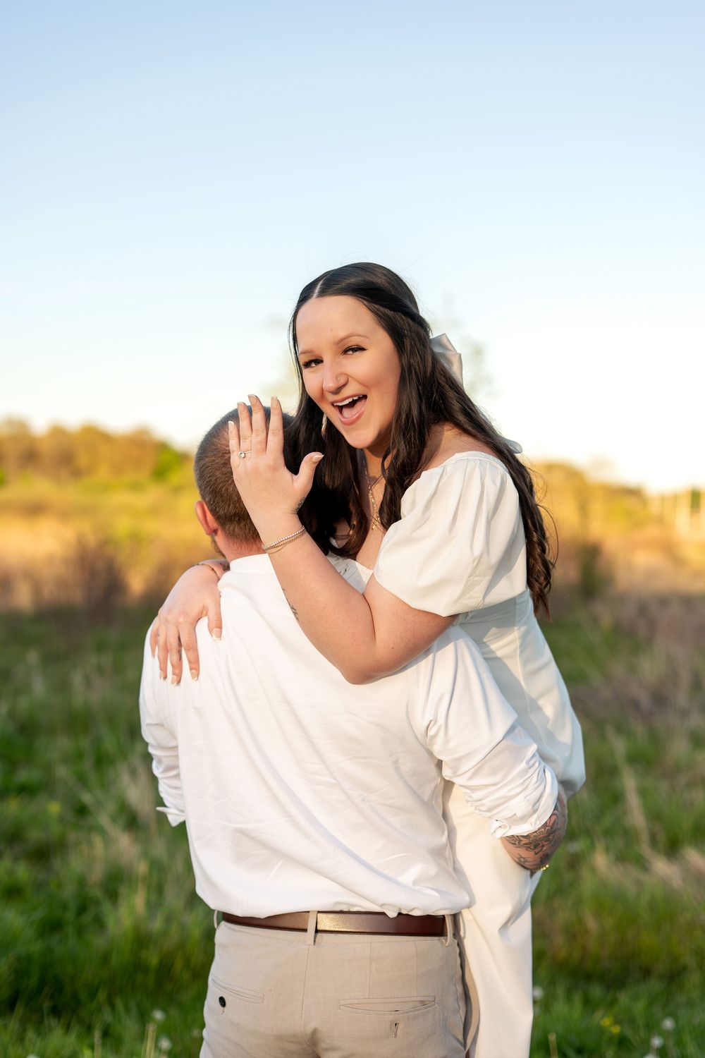Joyful woman laughing while embracing her partner outdoors in a sunny green field.
