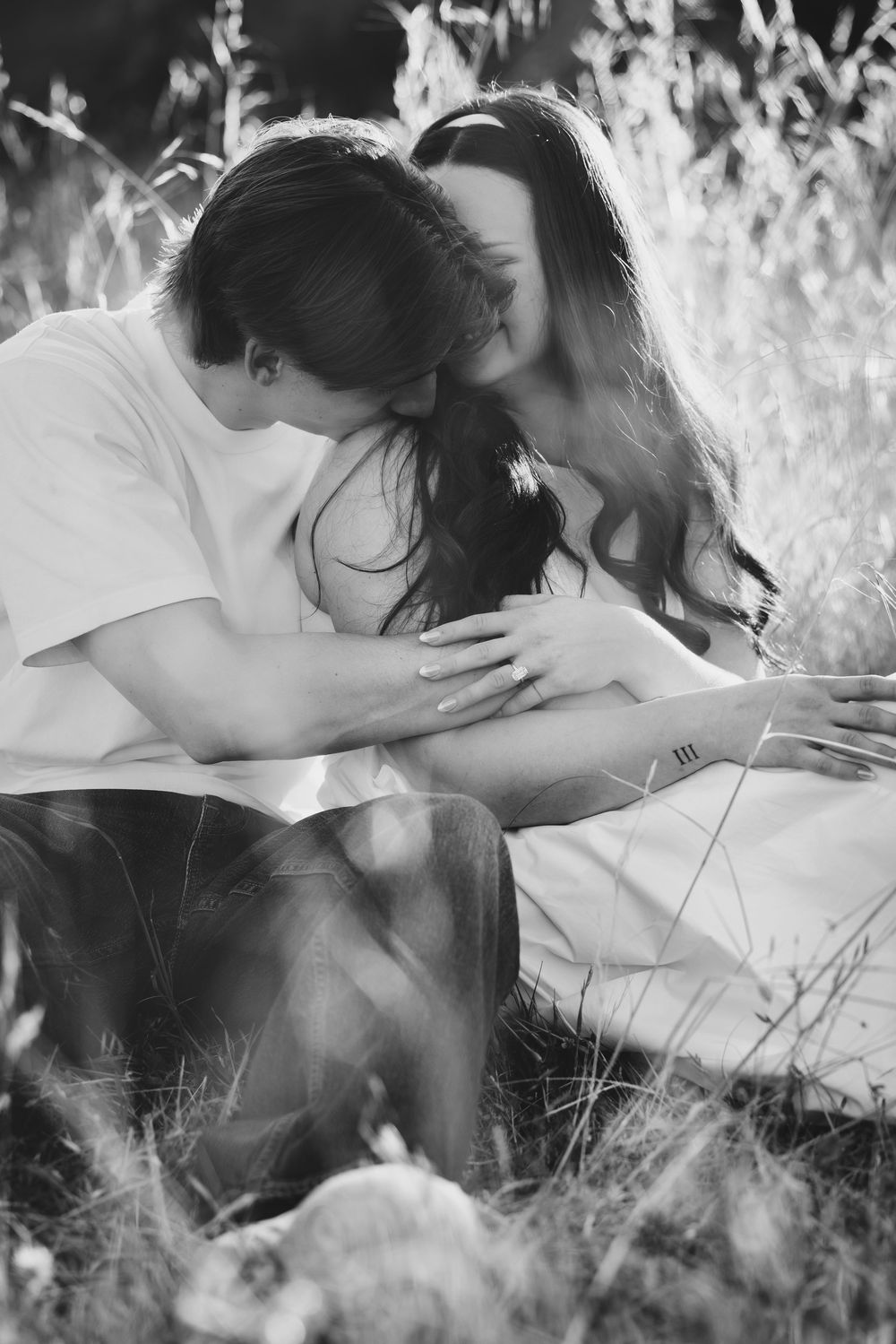 Black and white photo of a romantic couple embracing in a field of tall dry grass.