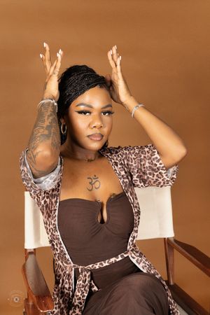 Woman in leopard print robe with Om tattoo poses in director's chair against brown background.