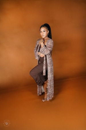 Stylish woman in leopard cardigan and brown pants strikes dynamic pose on orange backdrop.