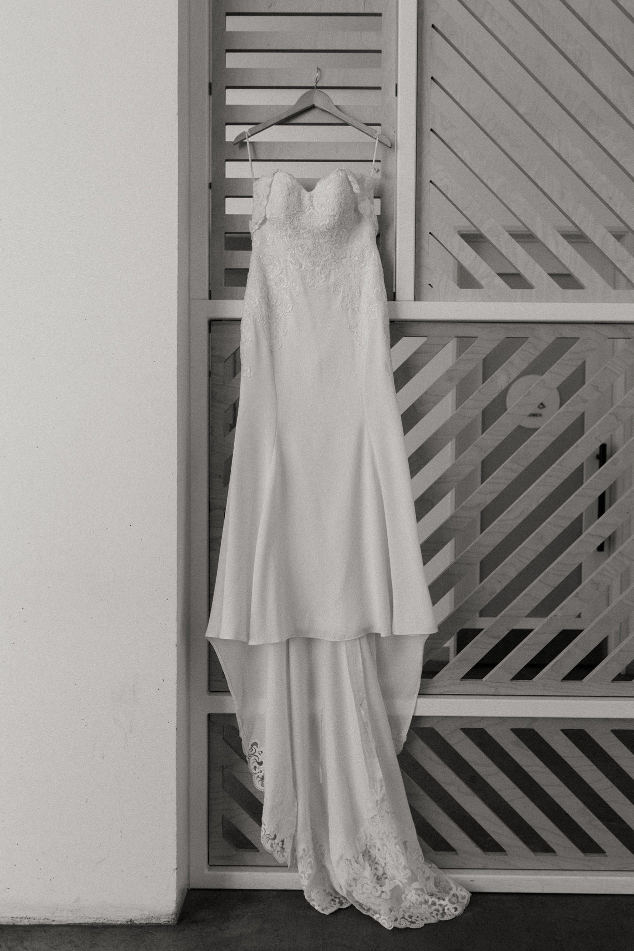 Elegant strapless wedding gown with lace bodice and train hanging on hanger against decorative shutters, black and white photo at The Lane.