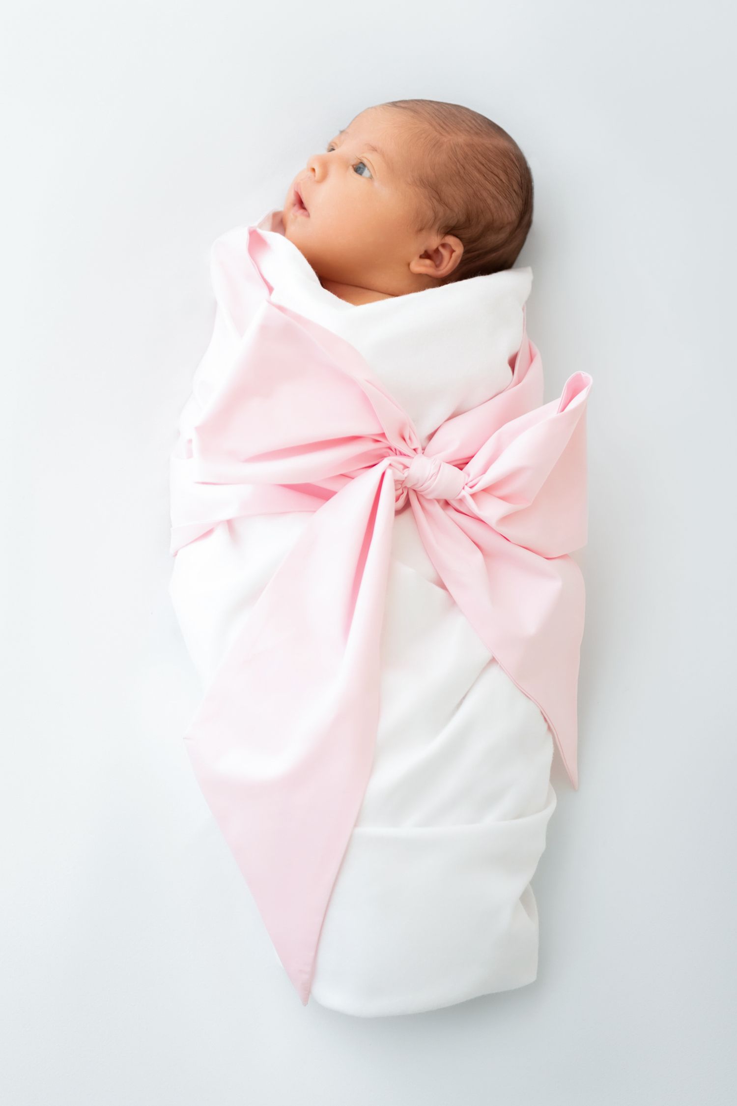 Baby girl wrapped in soft white fabric with a large pink bow during a minimalist studio newborn session in Winchester, VA