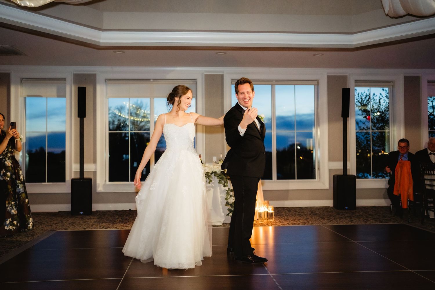 Bride and groom share first dance at elegant wedding reception with panoramic windows and warm lighting.