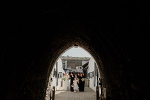 Bridal party walking through a stone archway tunnel at a charming whitewashed wedding venue.