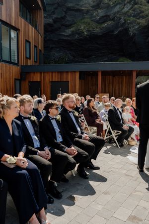 Wedding guests seated outdoors at a coastal venue ceremony on a sunny day.