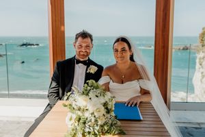 Bride and groom signing wedding register with stunning ocean view through floor-to-ceiling windows.