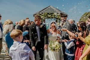 Newlyweds walking through confetti shower after outdoor wedding ceremony by the sea.