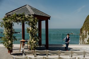 A floral-adorned gazebo overlooks the ocean at a scenic coastal wedding ceremony venue.