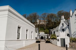 White rendered building exterior with hillside garden and blue sky in coastal town.