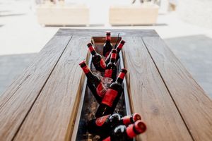 Red wine bottles chilling on ice in wooden table centerpiece at outdoor wedding.
